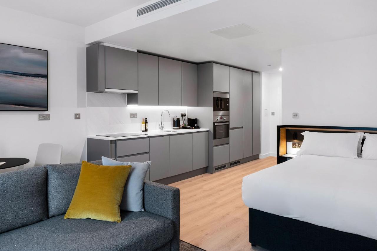 Citysuites 2 Aparthotel 曼彻斯特 外观 照片 The photo shows a modern studio apartment featuring an open-plan layout. On one side, there is a kitchenette with sleek, gray cabinets and appliances, including a coffee maker and oven. Adjacent to the kitchenette is a small dining area with a table 