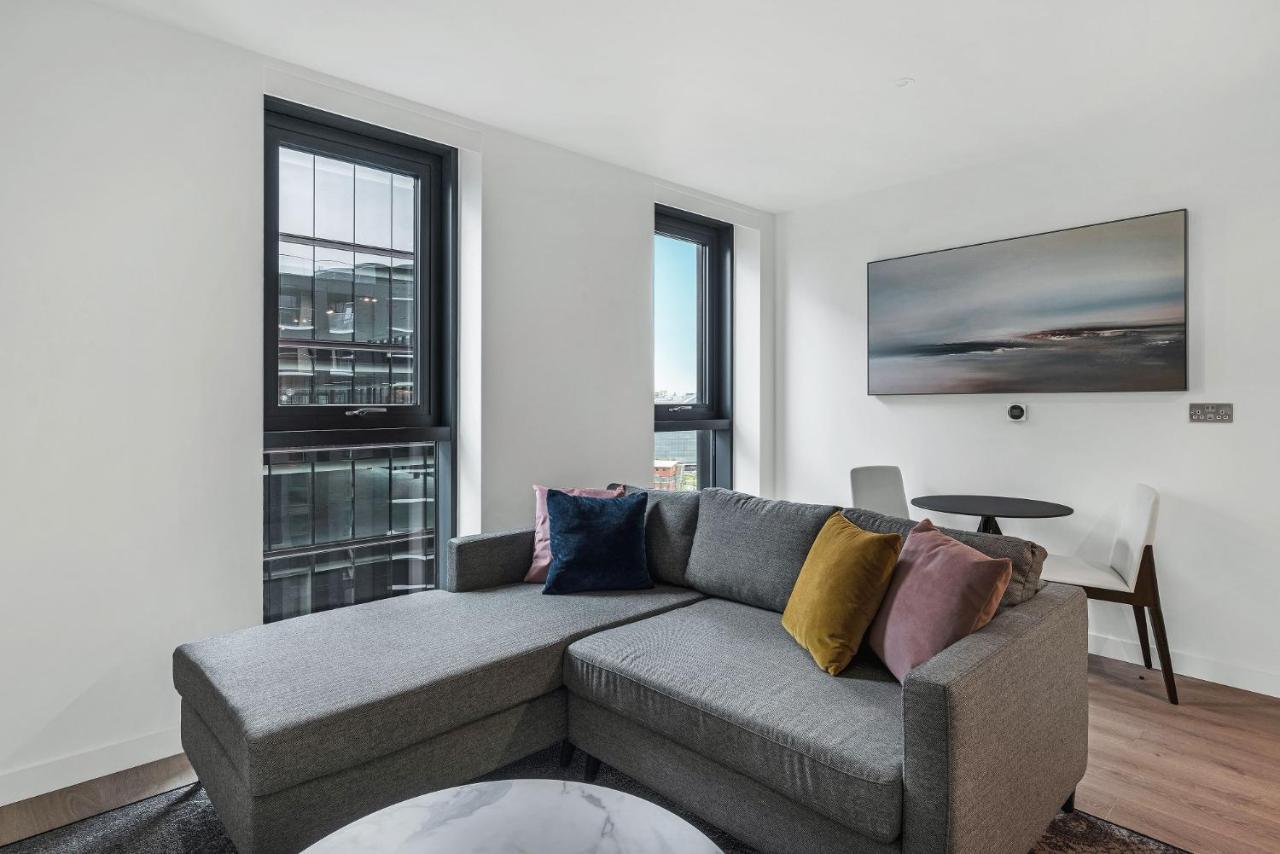 Citysuites 2 Aparthotel 曼彻斯特 外观 照片 The photo shows a modern living space featuring a gray sectional sofa adorned with colorful throw pillows. There are large windows allowing natural light to fill the room, offering a view of the outdoors. A wall-mounted television is positioned above