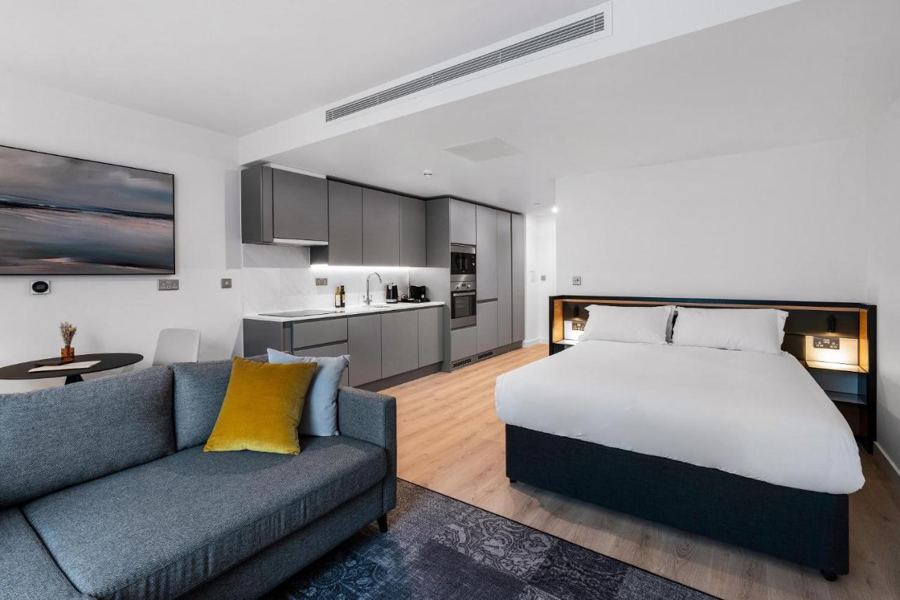 Citysuites 2 Aparthotel 索尔福德 外观 照片 The photo shows a modern studio apartment. On one side, there is a comfortable gray sofa adorned with a yellow cushion. Nearby, a round table is placed, likely intended for dining or casual sitting. 

The kitchen area features sleek gray cabinetry wi
