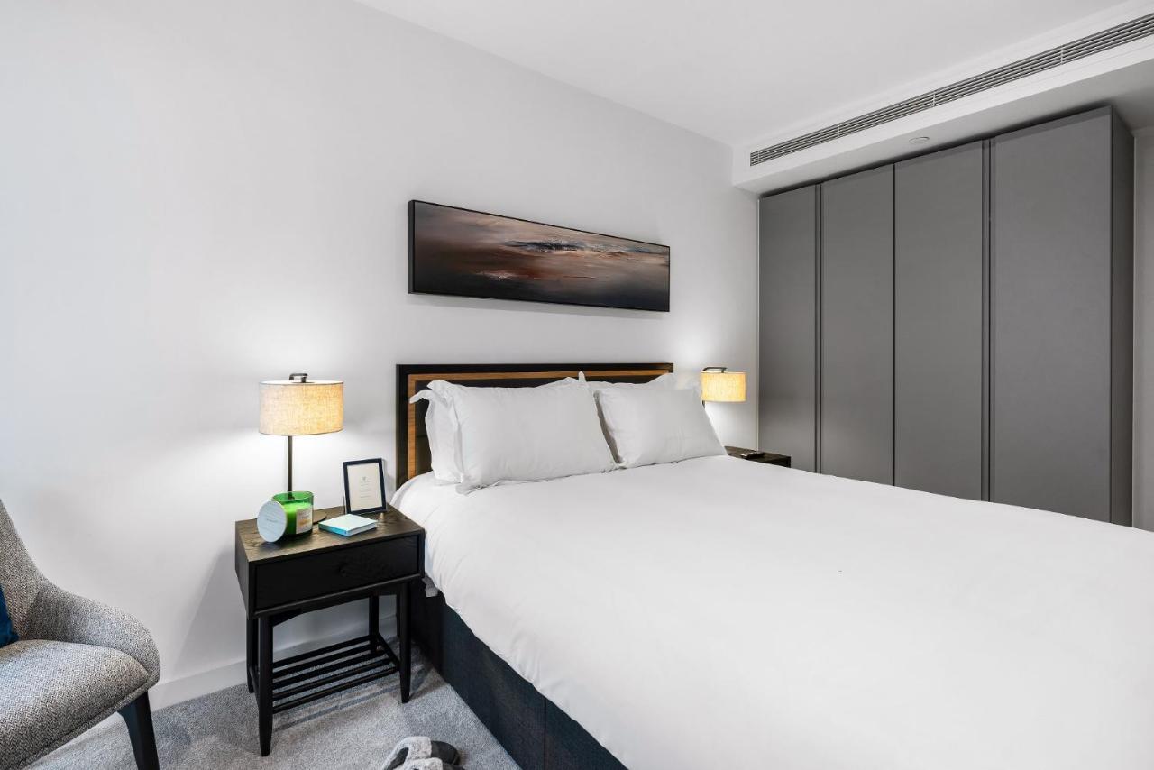 Citysuites 2 Aparthotel 索尔福德 外观 照片 The photo shows a modern bedroom with a neatly made bed featuring white linens and pillows. Flanking the bed are two bedside tables, each with a lamp providing soft lighting. There is a piece of artwork above the bed, which appears to depict a landsc