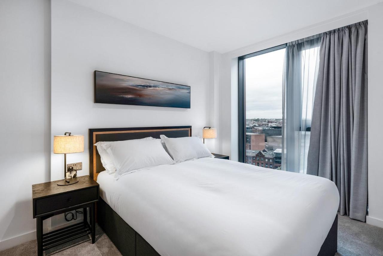 Citysuites 2 Aparthotel 曼彻斯特 外观 照片 The image shows a modern bedroom featuring a large bed with a white duvet and two pillows. On either side of the bed are small nightstands with lamps. A large window occupies one wall, draped with light gray curtains, allowing natural light to enter 
