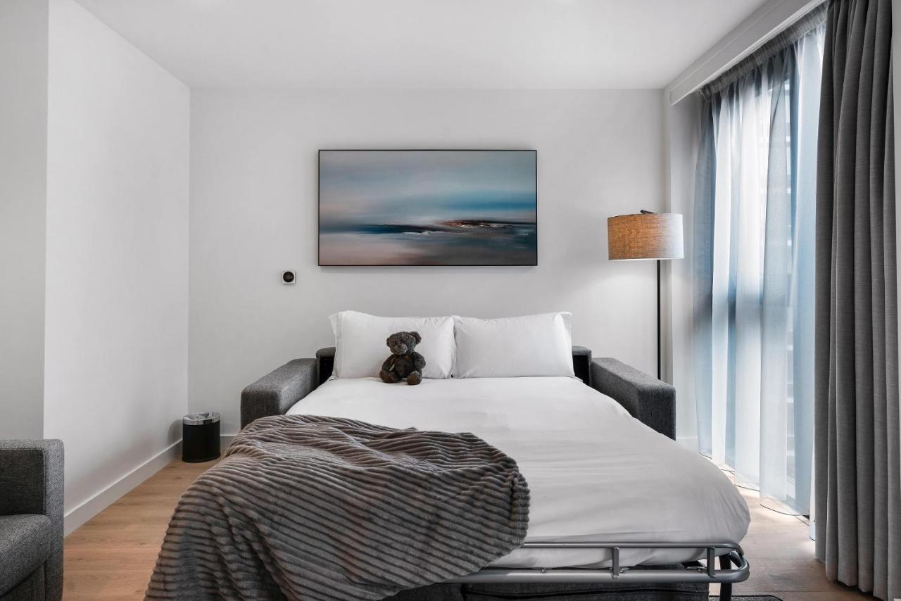 Citysuites 2 Aparthotel 曼彻斯特 外观 照片 The photo shows a modern bedroom featuring a bed with white bedding and a decorative throw blanket. There is a teddy bear placed on the bed. A piece of abstract art is hanging on the wall above the bed. The room has a large window with sheer curtains