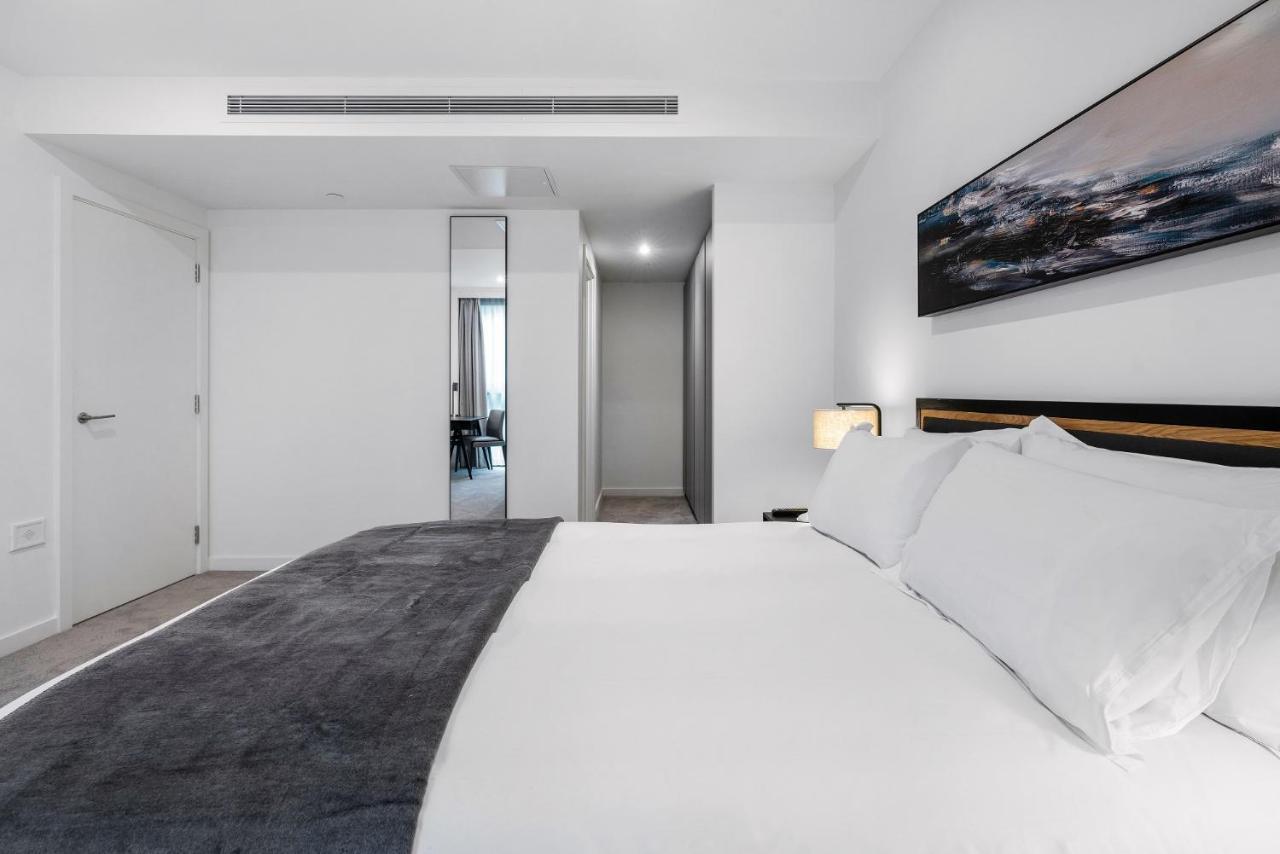 Citysuites 2 Aparthotel 曼彻斯特 外观 照片 The photo shows a modern bedroom with a minimalistic design. In the foreground, there is a neatly made bed with white linens and a dark gray throw blanket. To the side, there is a bedside lamp and a piece of abstract artwork on the wall above the bed