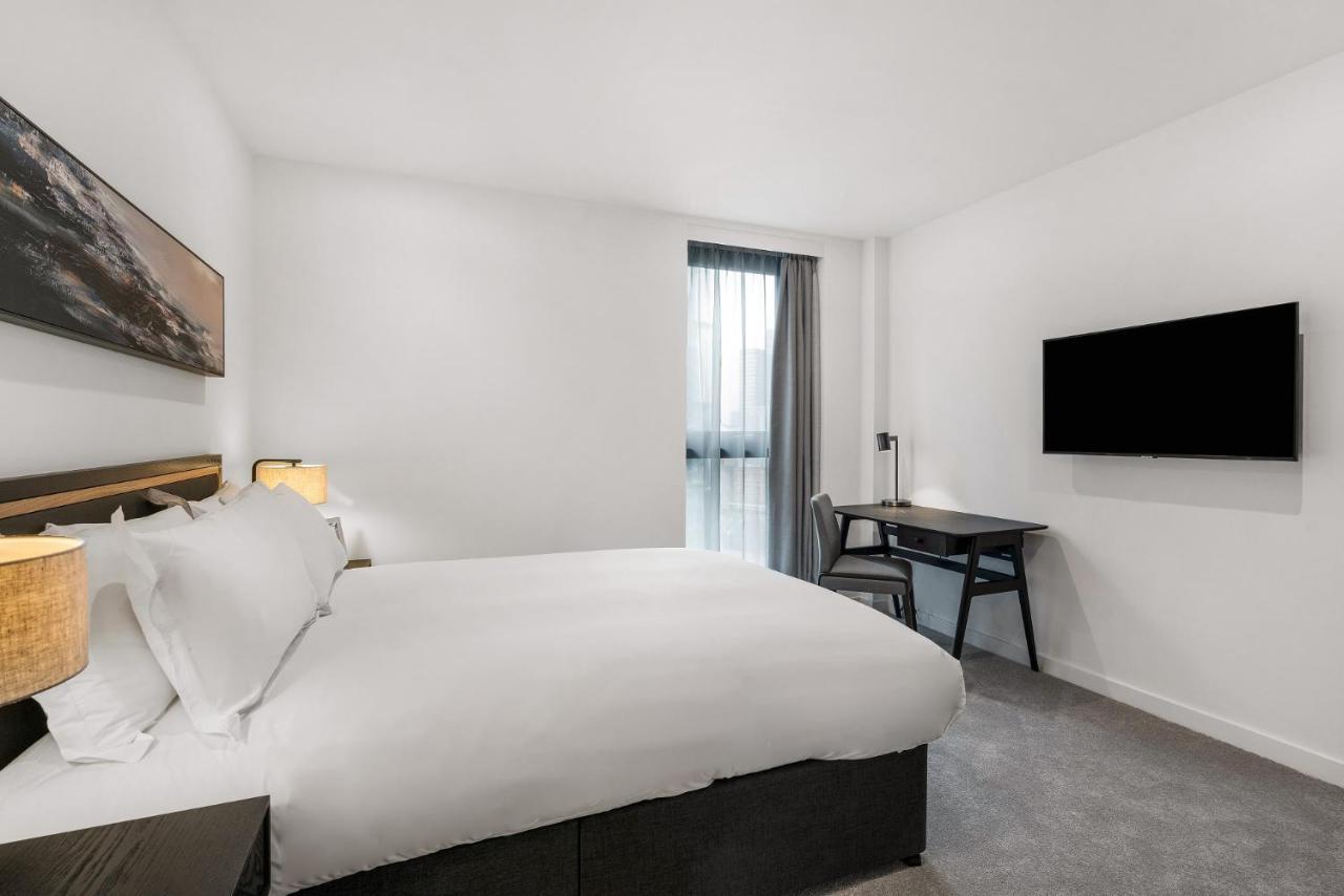Citysuites 2 Aparthotel 曼彻斯特 外观 照片 The photo shows a modern hotel room featuring a large bed with white linens and a dark headboard. There are two bedside lamps on either side of the bed. A desk with a chair is placed against one wall, and a flat-screen TV is mounted on another wall. 