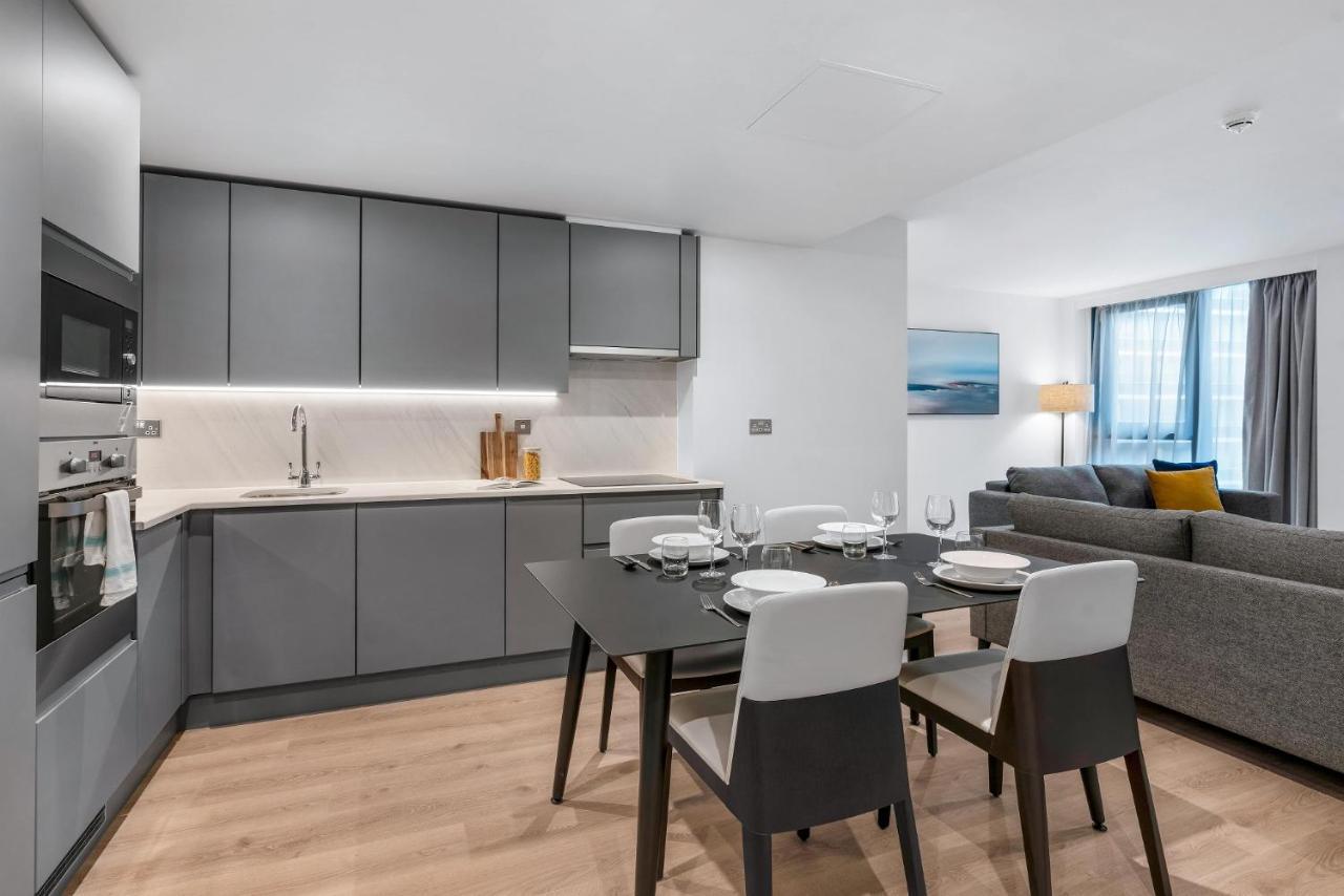 Citysuites 2 Aparthotel 曼彻斯特 外观 照片 The photo shows a modern, open-concept kitchen and living area. The kitchen features sleek, gray cabinetry with a countertop, a sink, and built-in appliances. There are cooking utensils displayed on the countertop. Next to the kitchen, there is a din