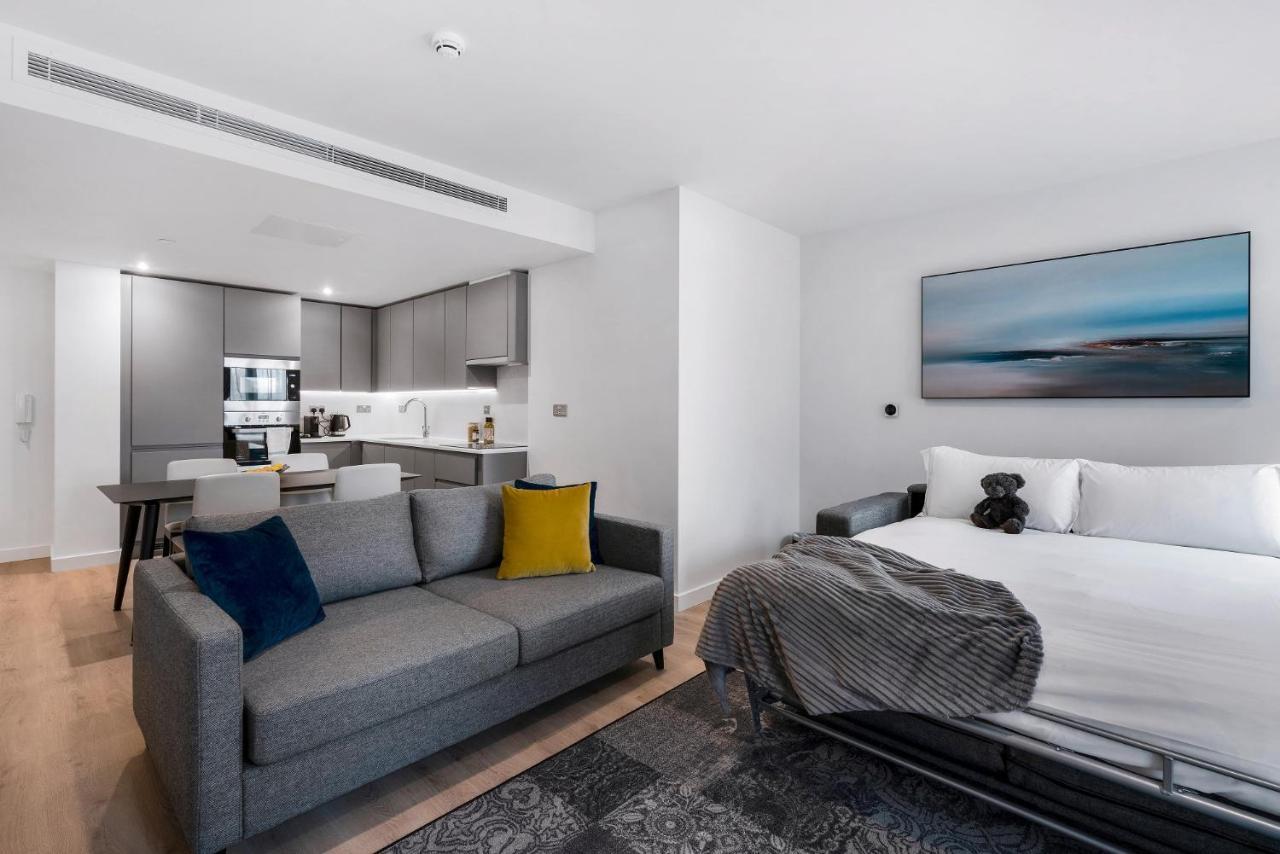Citysuites 2 Aparthotel 曼彻斯特 外观 照片 The photo shows a modern, open-concept living space that includes a kitchen and a sleeping area. 

- **Living Area**: On the left, there's a gray sofa with a blue and yellow throw pillow. A blanket is draped over one side, and there's a small dark ru