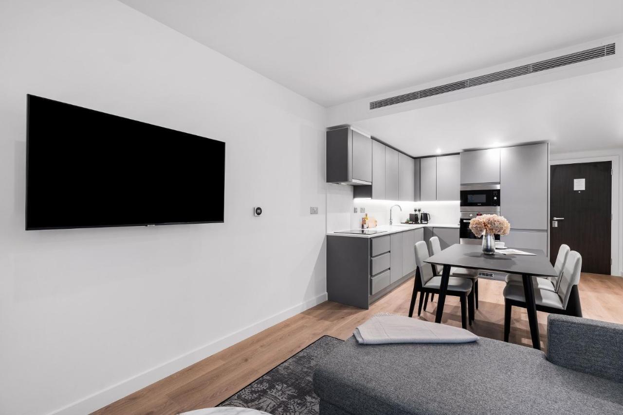 Citysuites 2 Aparthotel 索尔福德 外观 照片 The photo shows a modern, minimalist living space. On the left, there is a large flat-screen TV mounted on the wall. To the right, a kitchen area features sleek gray cabinets and appliances, including a built-in microwave. In front of the kitchen, th