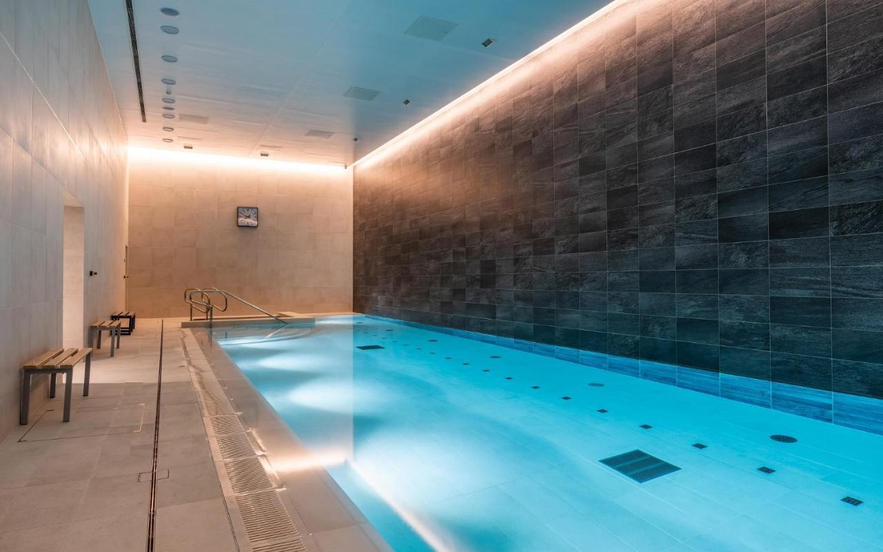 Citysuites 2 Aparthotel 曼彻斯特 外观 照片 The photo shows an indoor swimming pool area. The pool is illuminated with a soft blue light, creating a calming atmosphere. The walls are designed with dark tiles, and there is a lighter tiled area surrounding the pool. Ambient lighting is installed