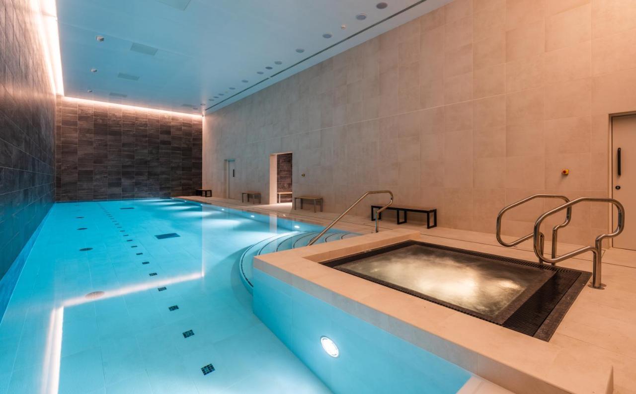 Citysuites 2 Aparthotel 曼彻斯特 外观 照片 The photo shows an indoor swimming pool area. The pool is a bright blue color and features smooth, tiled surfaces. On one side, there is a hot tub area with steps leading into it. The walls are made of light-colored stone, and there is ambient lighti