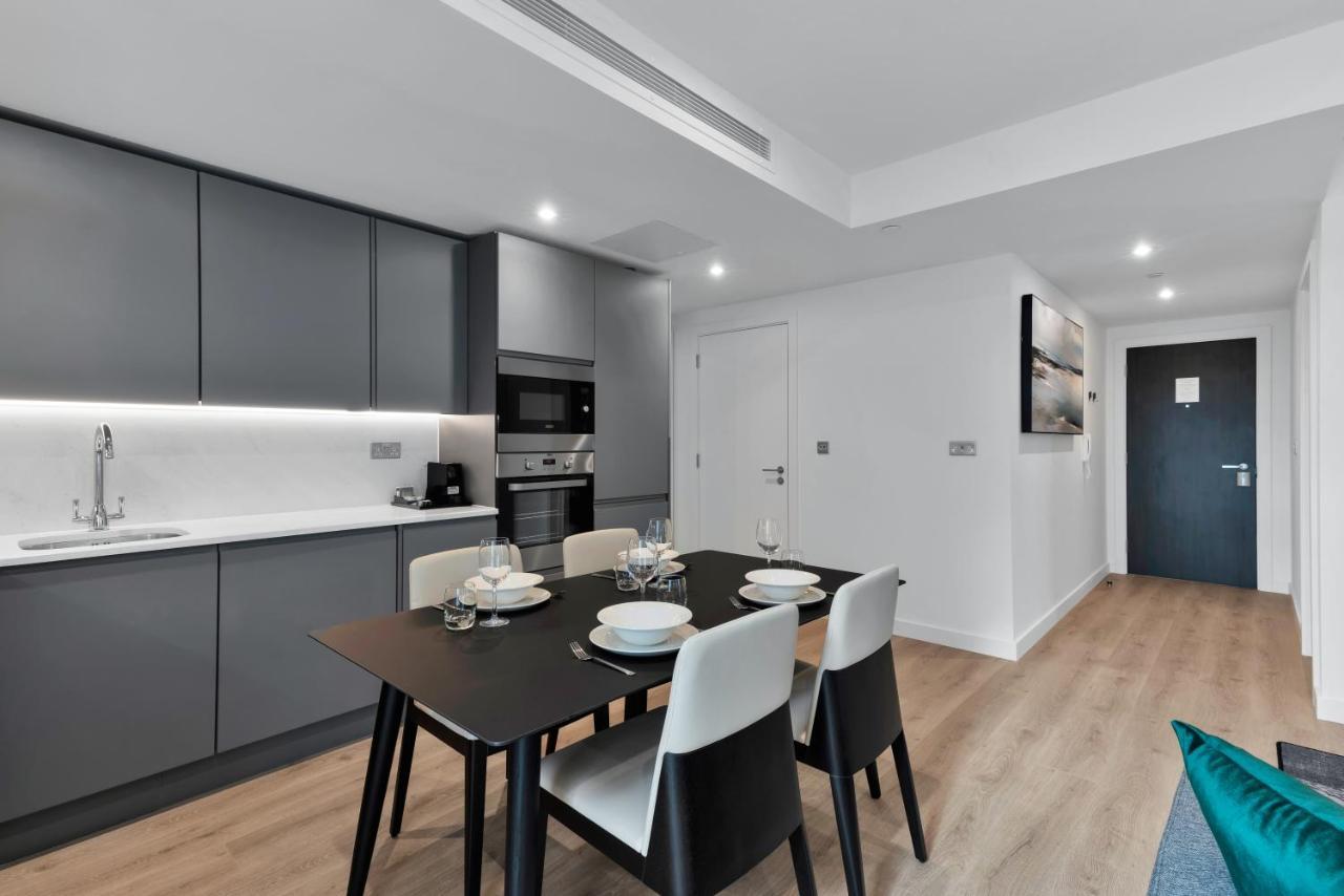 Citysuites 2 Aparthotel 曼彻斯特 外观 照片 The image shows a modern kitchen and dining area. The kitchen features sleek gray cabinets with a white countertop, and it is equipped with appliances such as a microwave. There’s a dining table set for four, with white plates and glasses ready. The 
