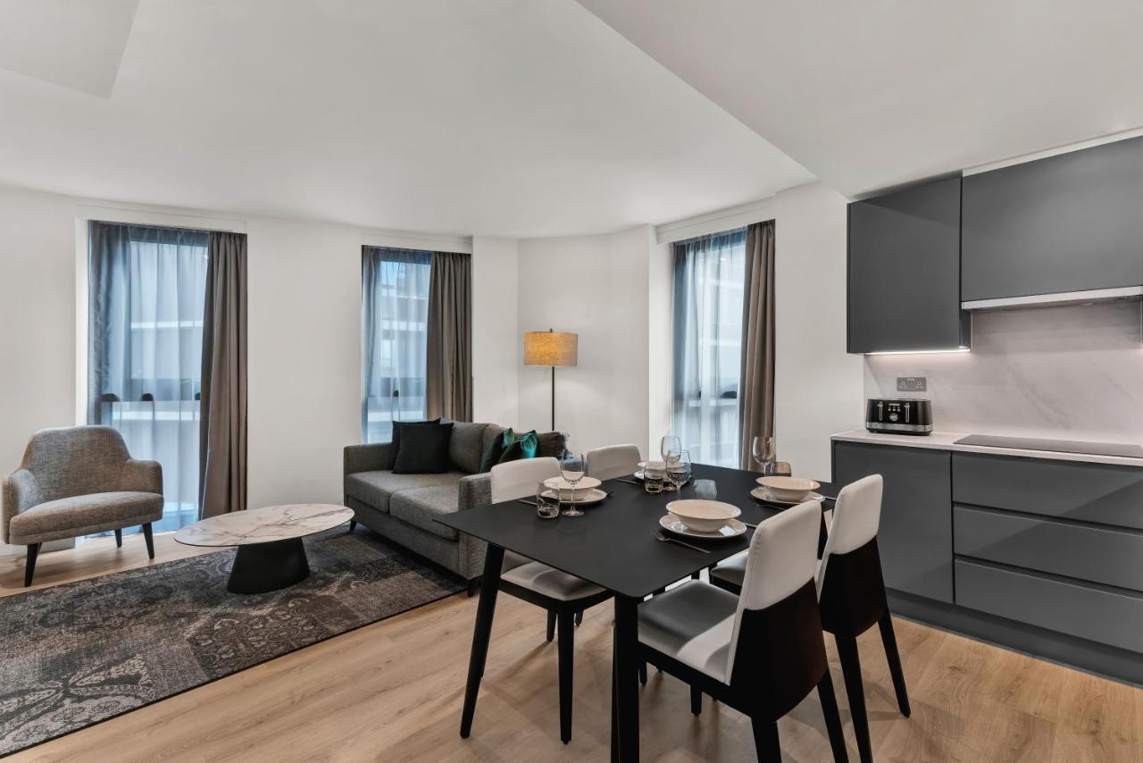 Citysuites 2 Aparthotel 曼彻斯特 外观 照片 The photo shows a modern living space that includes a dining area and a seating area. There's a sleek black dining table set with plates and cutlery, accompanied by white and black chairs. To one side, a comfortable gray sofa faces the dining area, c