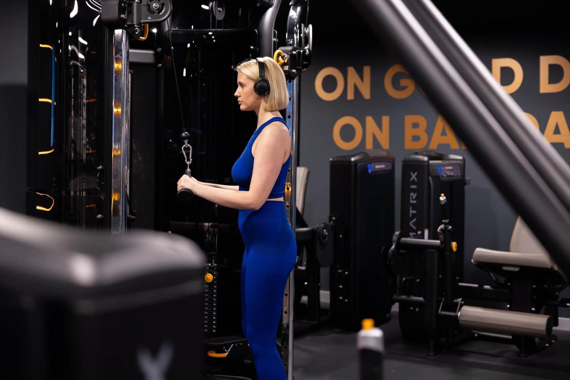 Citysuites 2 Aparthotel 曼彻斯特 外观 照片 The photo shows a woman working out in a gym. She is wearing a blue athletic outfit and headphones while using a gym machine. The background features various other gym equipment and a wall with the words "ON GOOD ON BAD" displayed prominently. The se