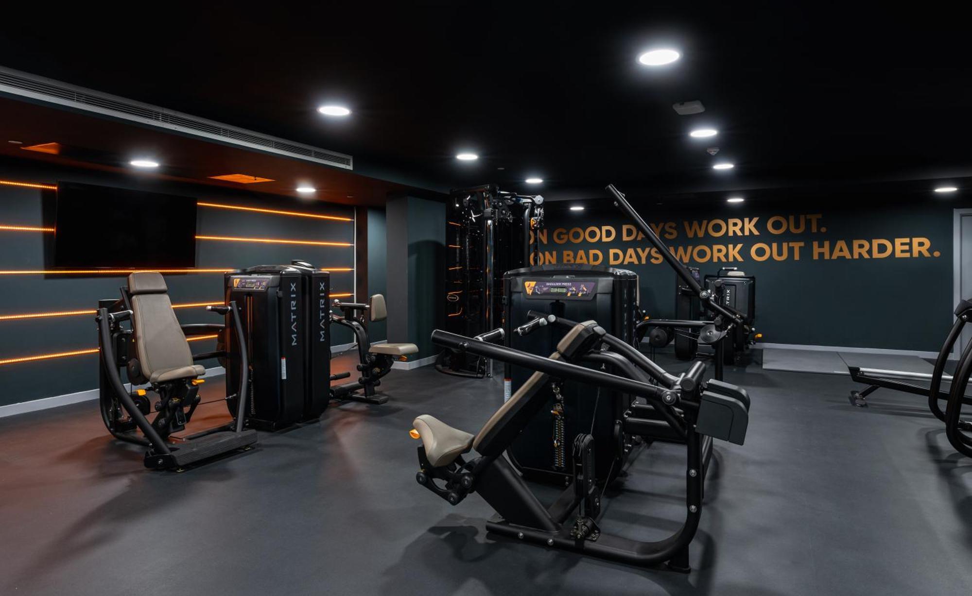 Citysuites 2 Aparthotel 曼彻斯特 外观 照片 The photo shows a modern gym interior. The gym features various exercise machines, including weight training equipment. The flooring is dark, and the walls are adorned with motivational text that reads, "ON GOOD DAYS WORK OUT. ON BAD DAYS WORK OUT HA