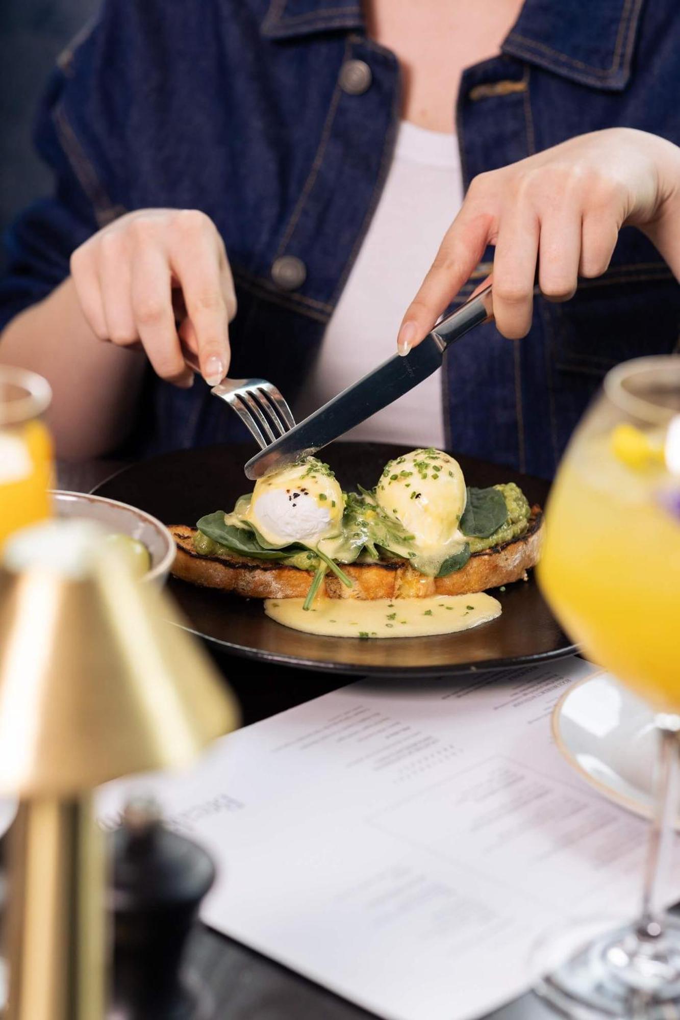 Citysuites 2 Aparthotel 曼彻斯特 外观 照片 The photo shows a person preparing to eat a dish of eggs Benedict. They are holding a knife and fork, ready to cut into the meal, which features poached eggs on top of a slice of toast, accompanied by spinach and a creamy hollandaise sauce drizzled o