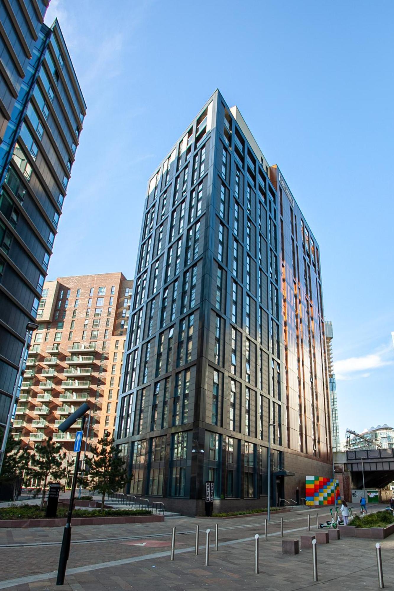 Citysuites 2 Aparthotel 索尔福德 外观 照片 The photo shows a modern high-rise building with a sleek, glass façade. It is set against a blue sky, indicating a clear day. The building appears to have multiple floors with large windows that reflect light. Nearby, there are additional buildings, 